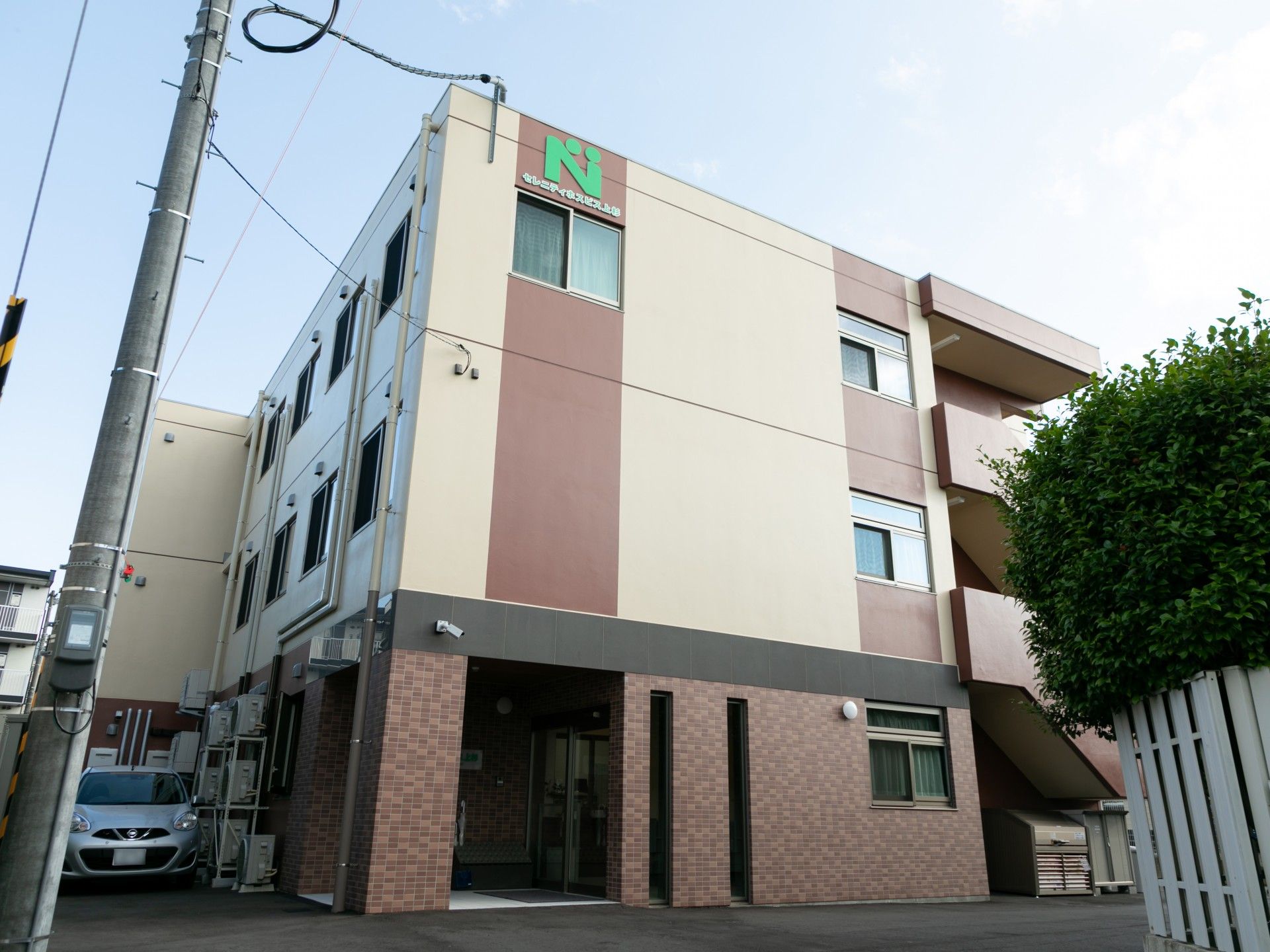ブラウンとベージュの外壁の3階建ての建物の側面には屋外階段も設置され、エヌの文字が書かれている。
