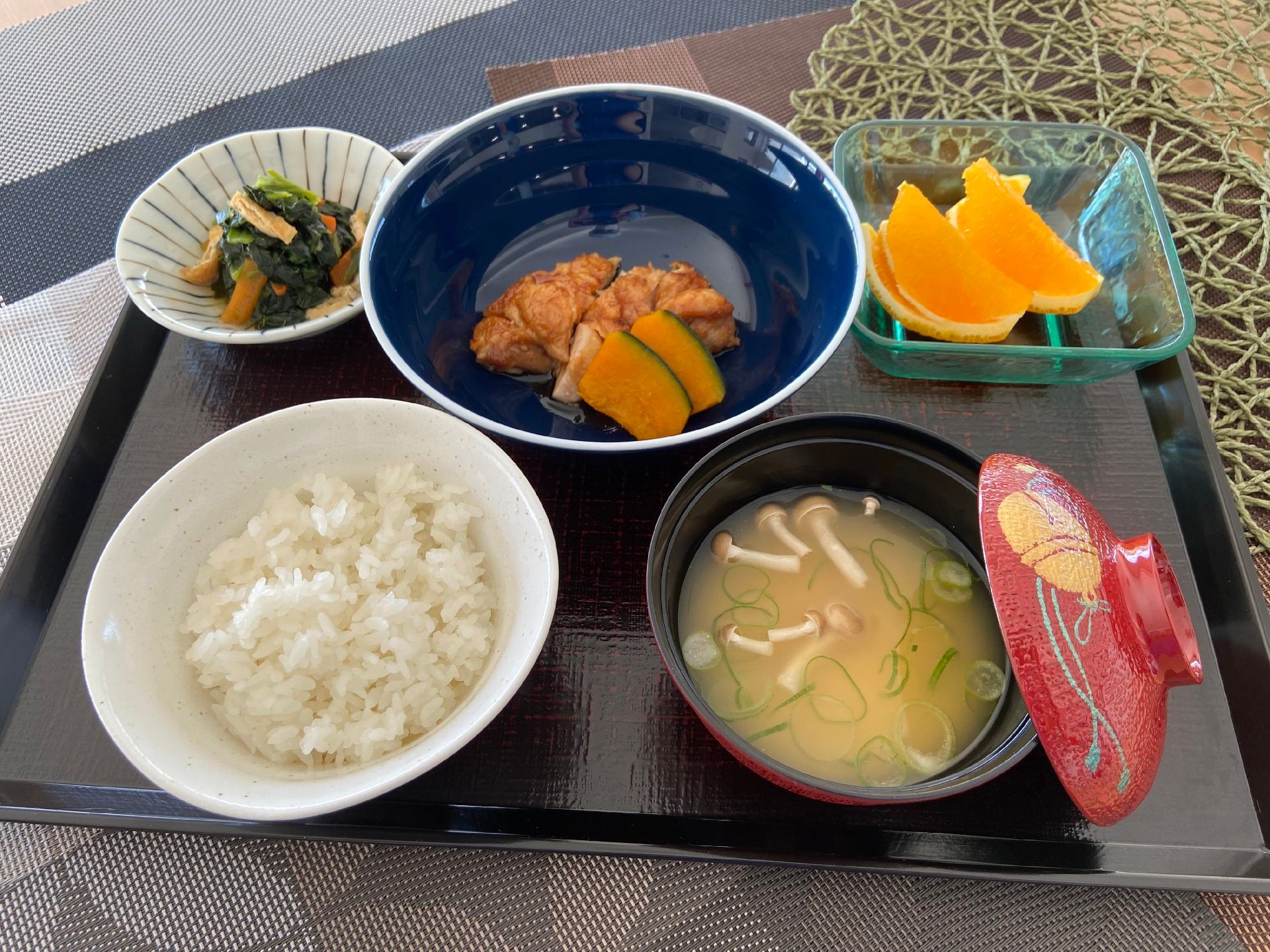 白いご飯に味噌汁、かぼちゃと鶏肉の煮物、青菜のお浸しなどにオレンジが添えられている。