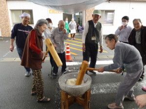 餅つきを楽しそうにしている高齢者たち、タオルを頭に巻いたスタッフもいる。