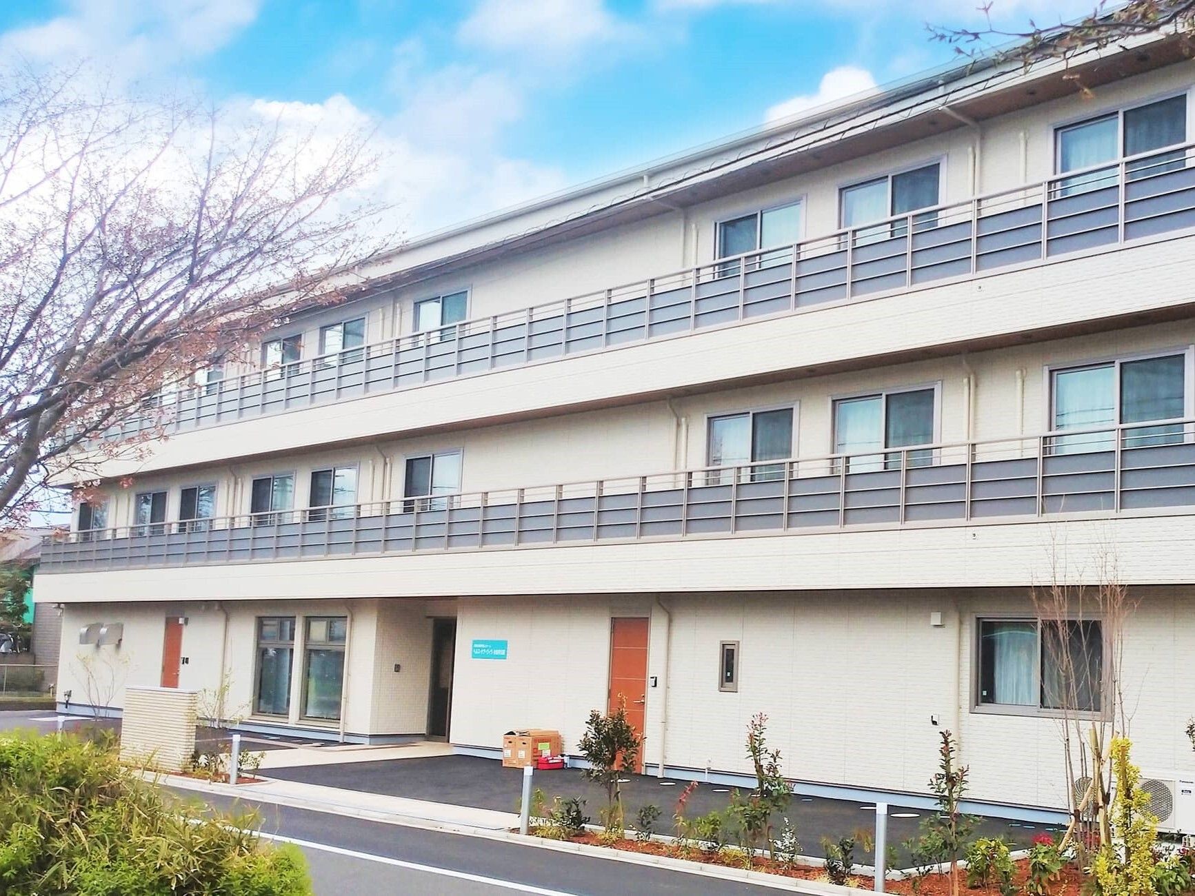 各フロアにベランダがあり、白を基調とした3階建ての建物周りには草木が植えられている。