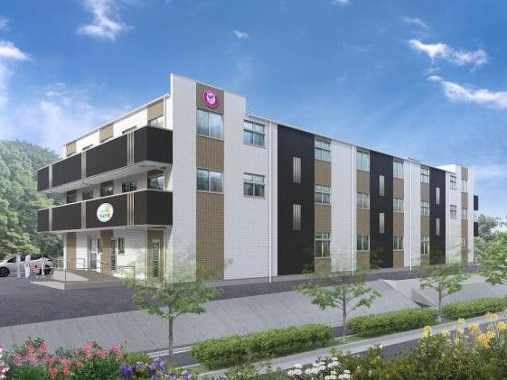 白を基調とした3階建ての建物にはブラウンやダークグレーのアクセントが付き、敷地内には駐車場がある。