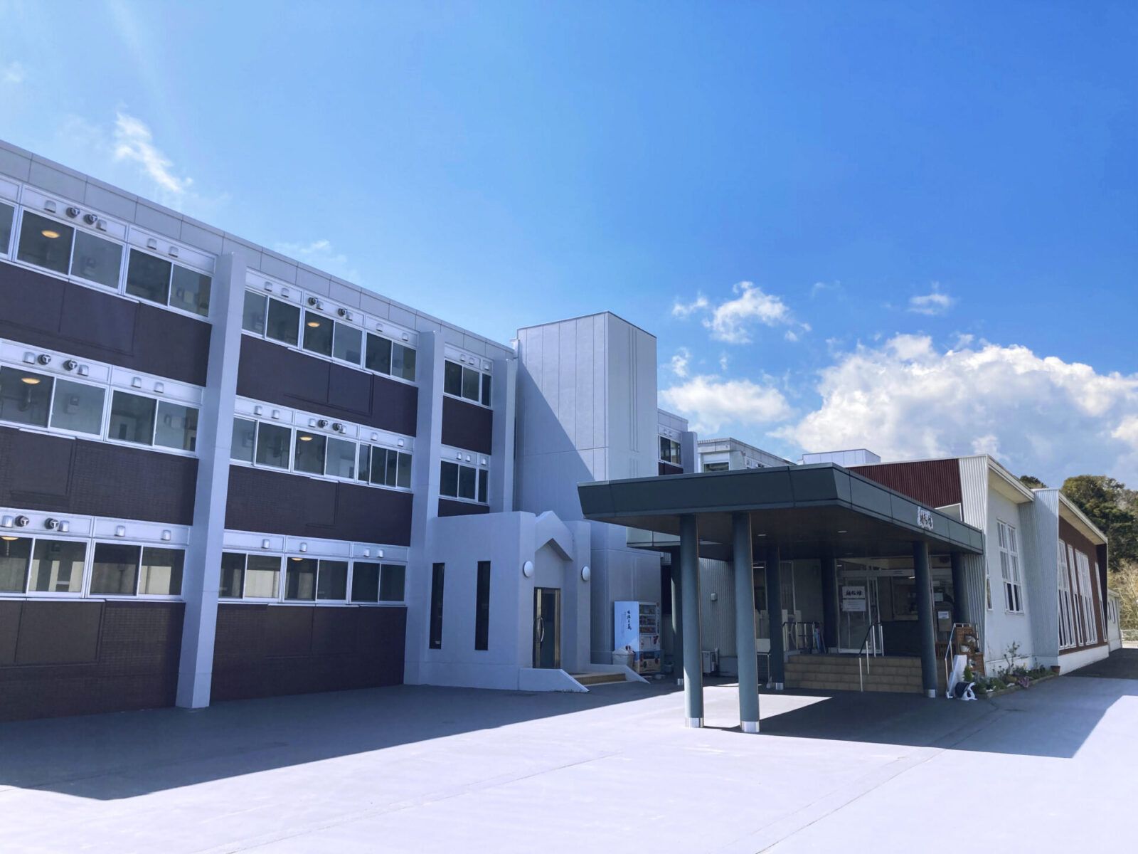 日当たりのいい場所に建っている3階建ての建物の外壁はグレーと黒。玄関には車寄せが付いている。