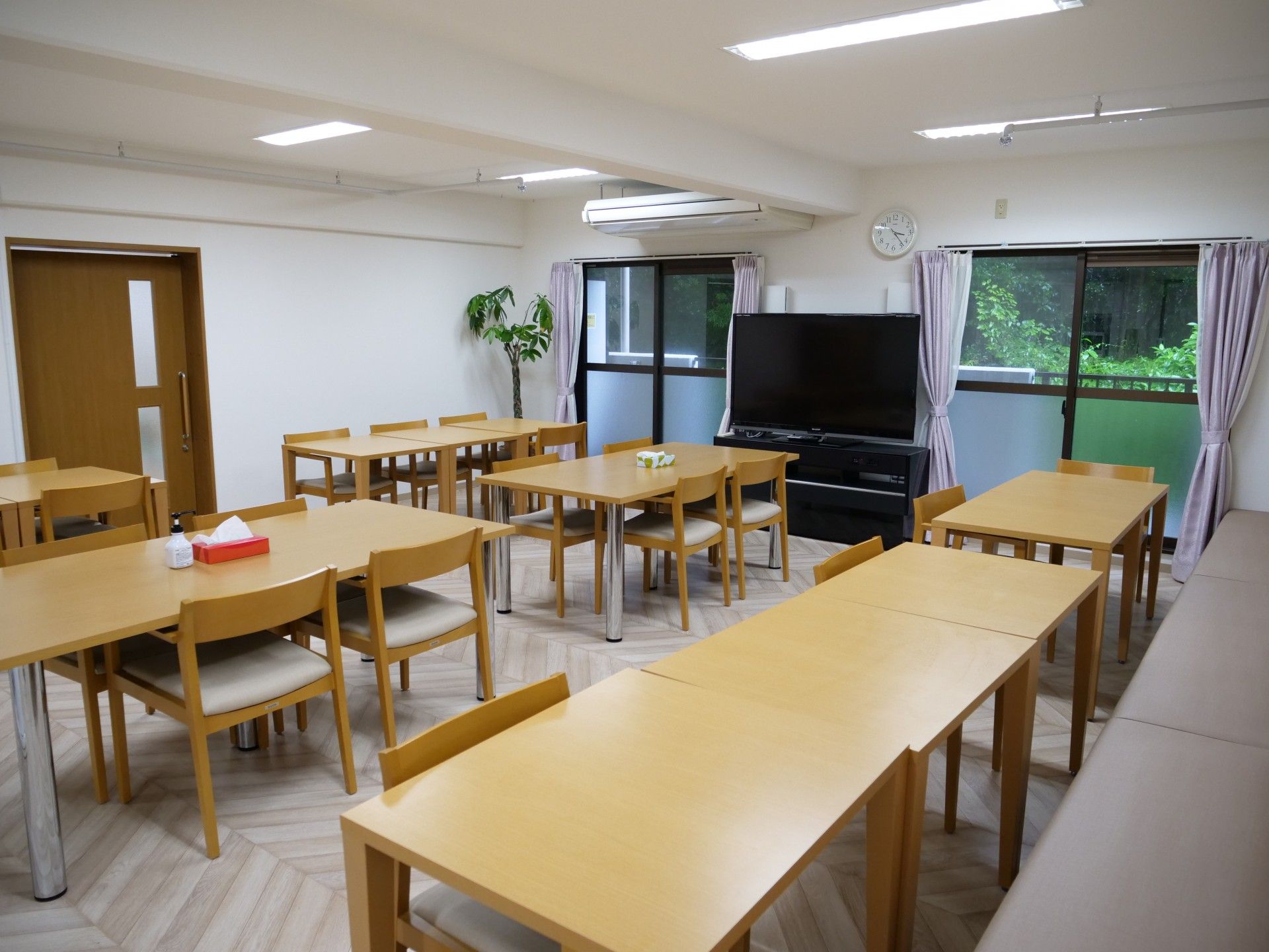 緑の多い屋外で笑顔で過ごしている車いすの高齢女性とエプロンを付けた男性スタッフ。
