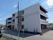 白を基調とした建物は３階建てで各フロアにベランダがあり、道路に面して建っている。