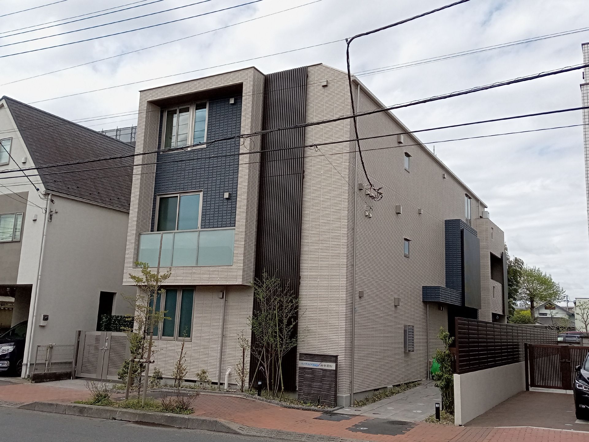 ベージュやグレーの建物は道路に面して建っている。周りには草木が植えられている。