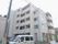白を基調とした大きな建物の前には草木が植えられている。ブルーと白の館銘板もある。