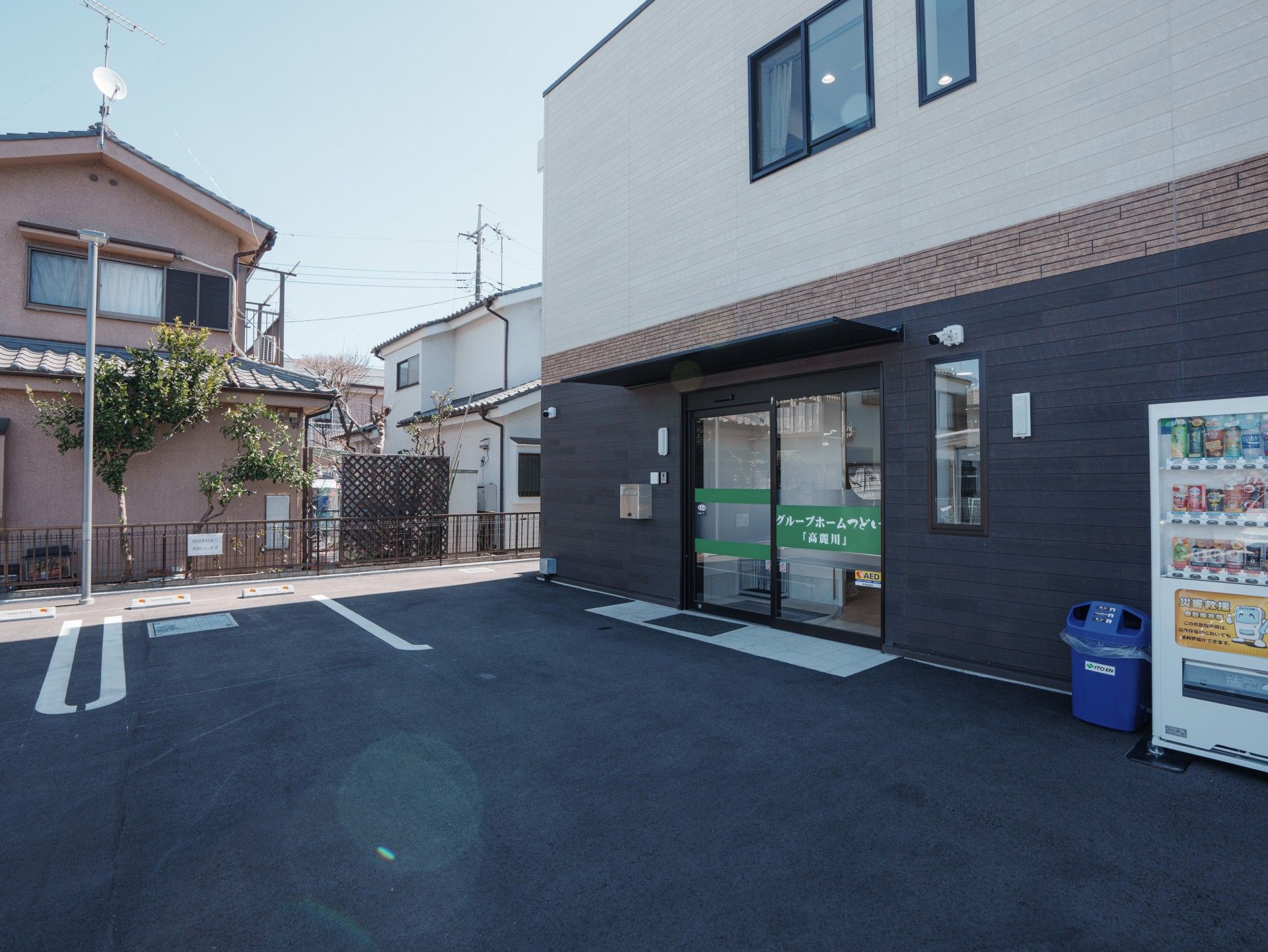 ベージュとブラウンの２階建ての建物は日当たり良好で横に長く、玄関には手すり付きのスロープがある。