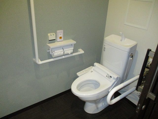 手すり付きのトイレは広く、スライド式のドアが設置され、オレンジの呼び出しボタンもある。