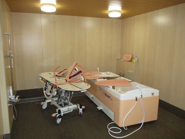 白とピンクの寝台浴が設置された浴室は広く、介助スペースは広い。ストレッチャータイプのリフトがある。