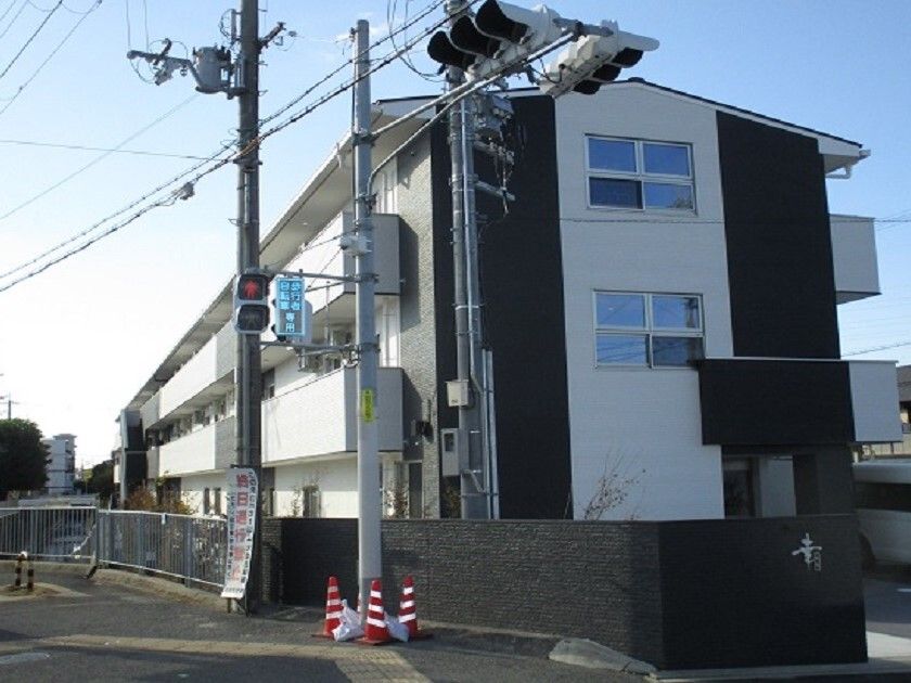 白とダークグレーの3階建ての建物の各フロアにベランダがあり、日当たりのいい場所に建っている。