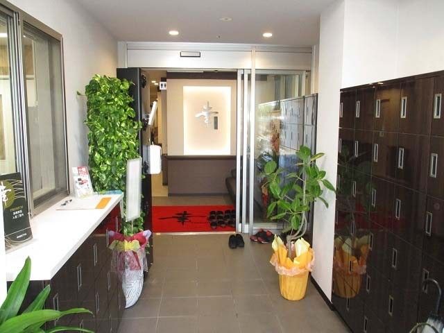 玄関には観葉植物が多く飾られ、扉付きの背の高さが異なる靴箱が置かれ、赤いマットが敷かれている。