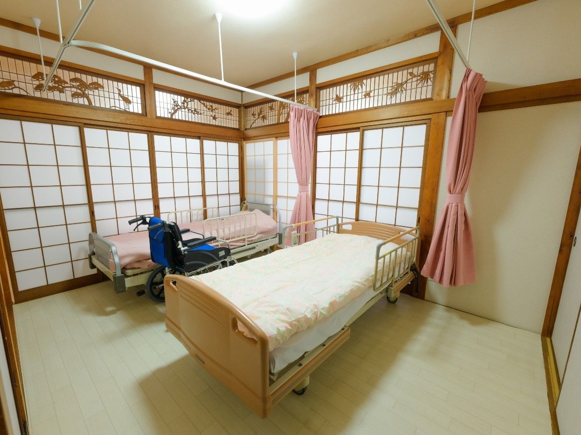 笑顔で緑の多い場所を散歩している車いすの高齢女性と付き添いのエプロンを付けた女性スタッフ。