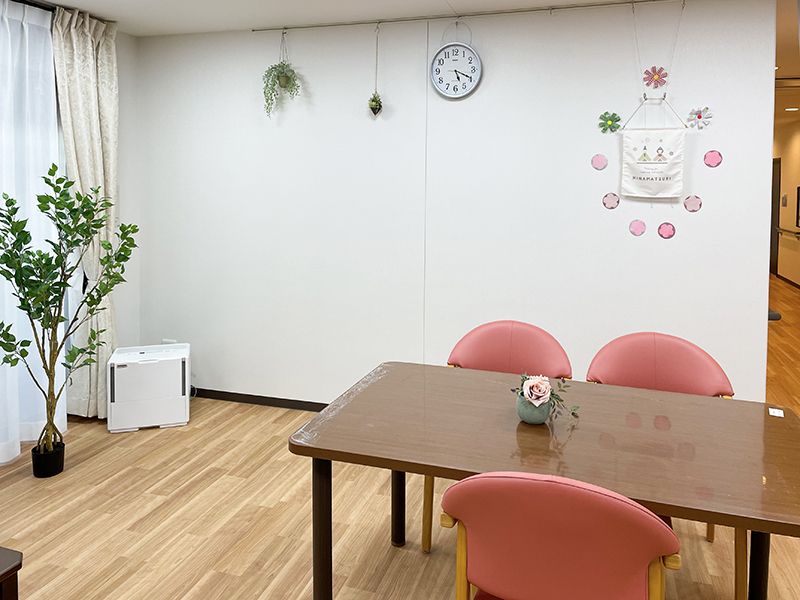 観葉植物が飾られているフローリングの共有スペースには木製のダイニングテーブルが置かれている。