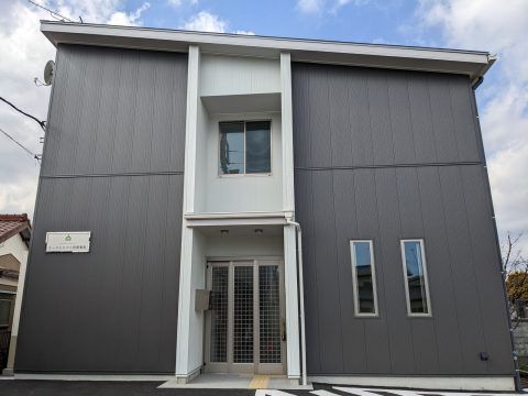 ダークグレーと白の外壁の２階建ての建物は玄関のそばにポストが付き、駐車場も付いている。