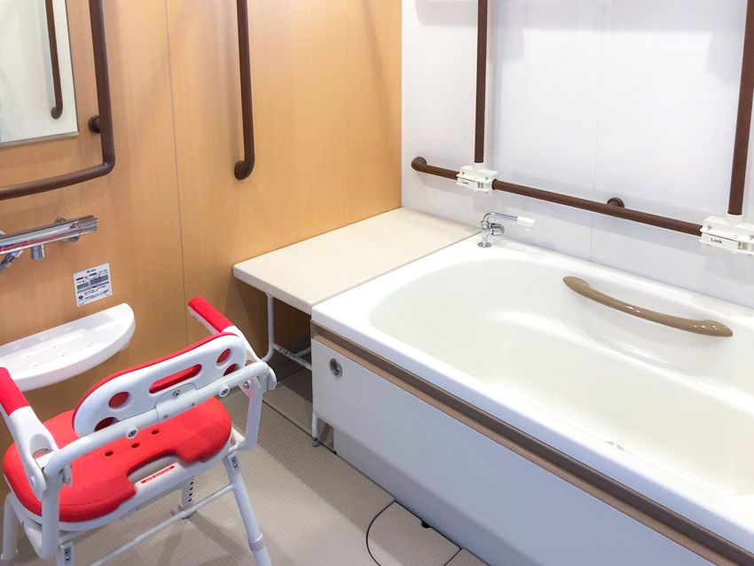 手すりがたくさん付いた一人用の浴槽が設置された浴室にはシャワーもあり、ベンチも置かれている。