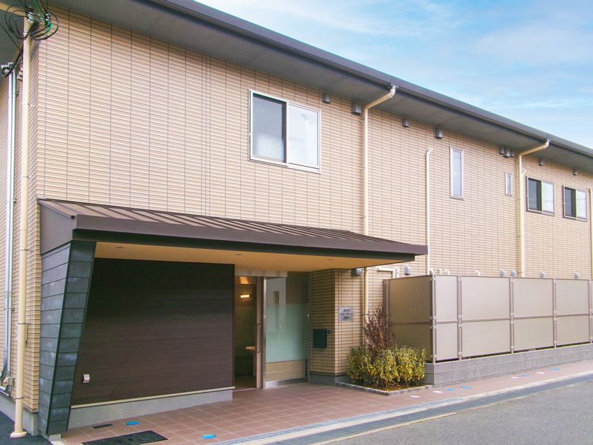 横に長いブラウン系の建物は2階建てで玄関には大きな車寄せが付き、明るい雰囲気。