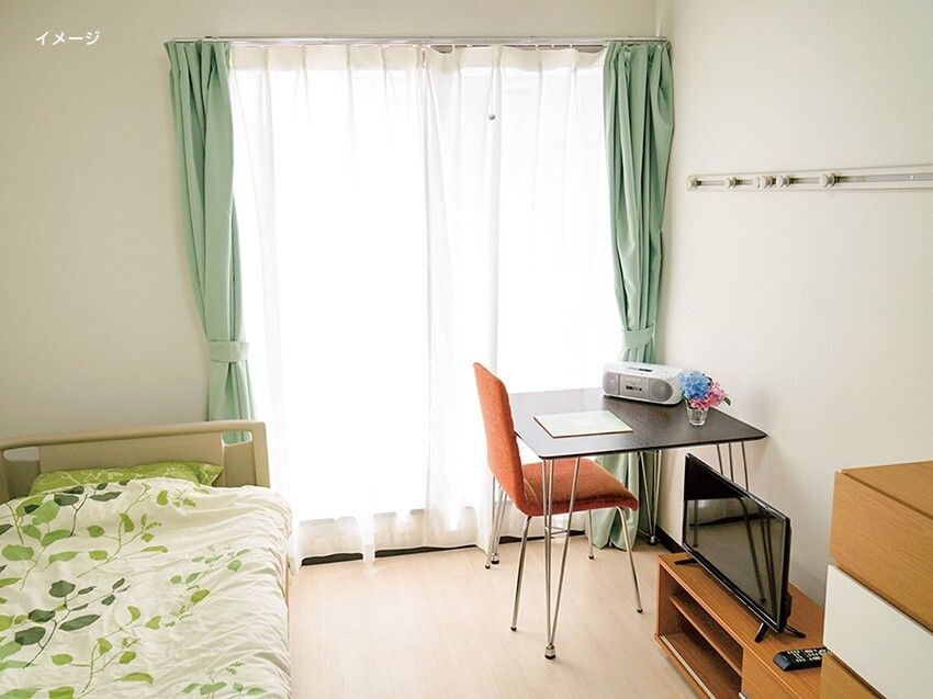 大きな窓が付いたフローリングの部屋には寝具付きのベッドやデスクセットがあり、明るい雰囲気。