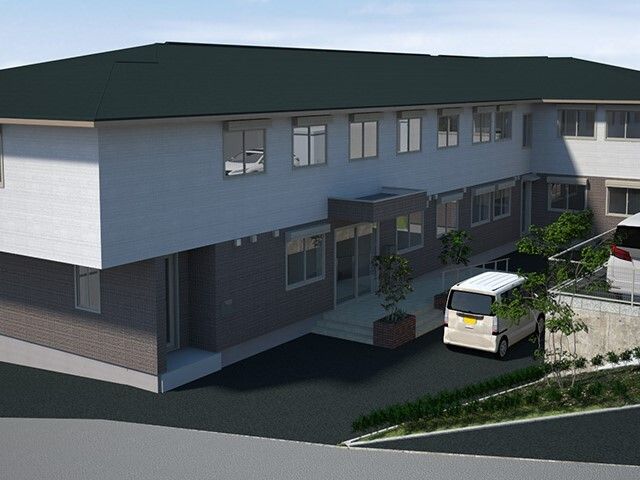 グレーの屋根が付いた２階建ての建物は敷地内に草木が植えられ、駐車場があり、窓もたくさん付いている。