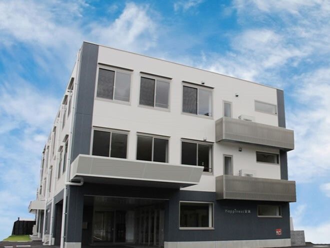 大きな車寄せが付いた3階建ての建物の外壁は白とダークグレー。各フロアにベランダもある。