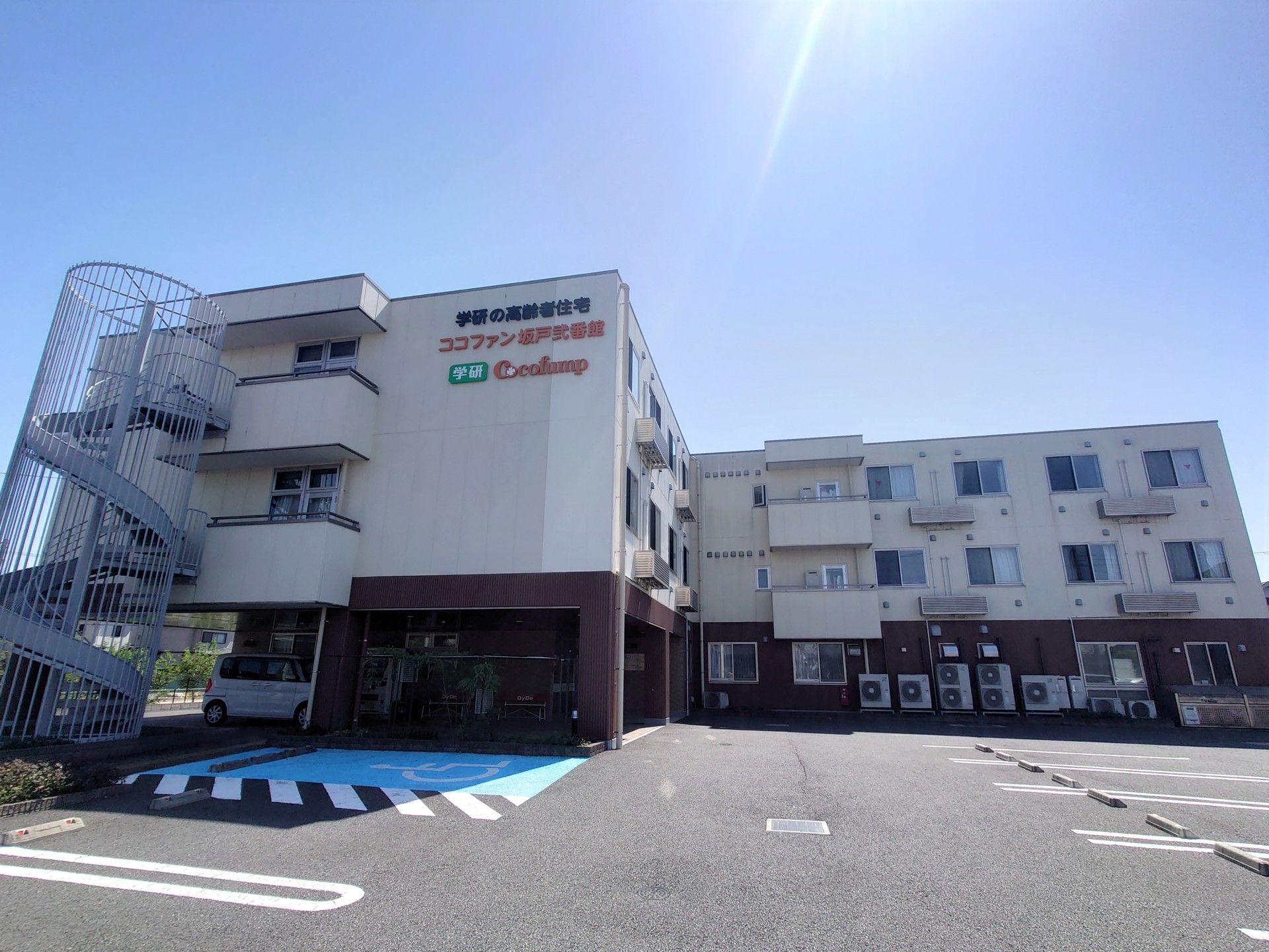 広い駐車場があり、外壁にココファン坂戸弐番館と書かれている3階建ての建物。