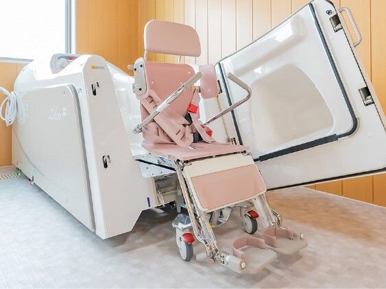座ったまま入浴できる白とピンクの機械浴が設置されている広い浴室には大きな窓がある。