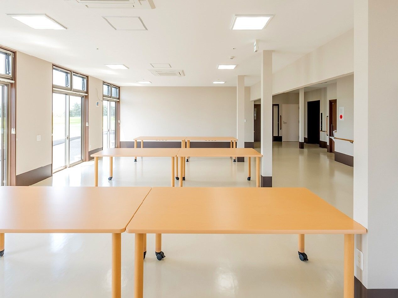椅子がセットされていないダイニングテーブルセットが複数置かれている広い食堂。