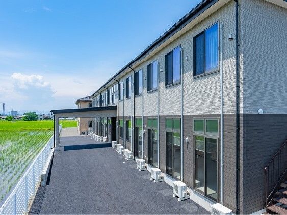 田んぼに囲まれている２階建ての建物は日当たりのいい場所に建っていて、玄関には車寄せが付いている。