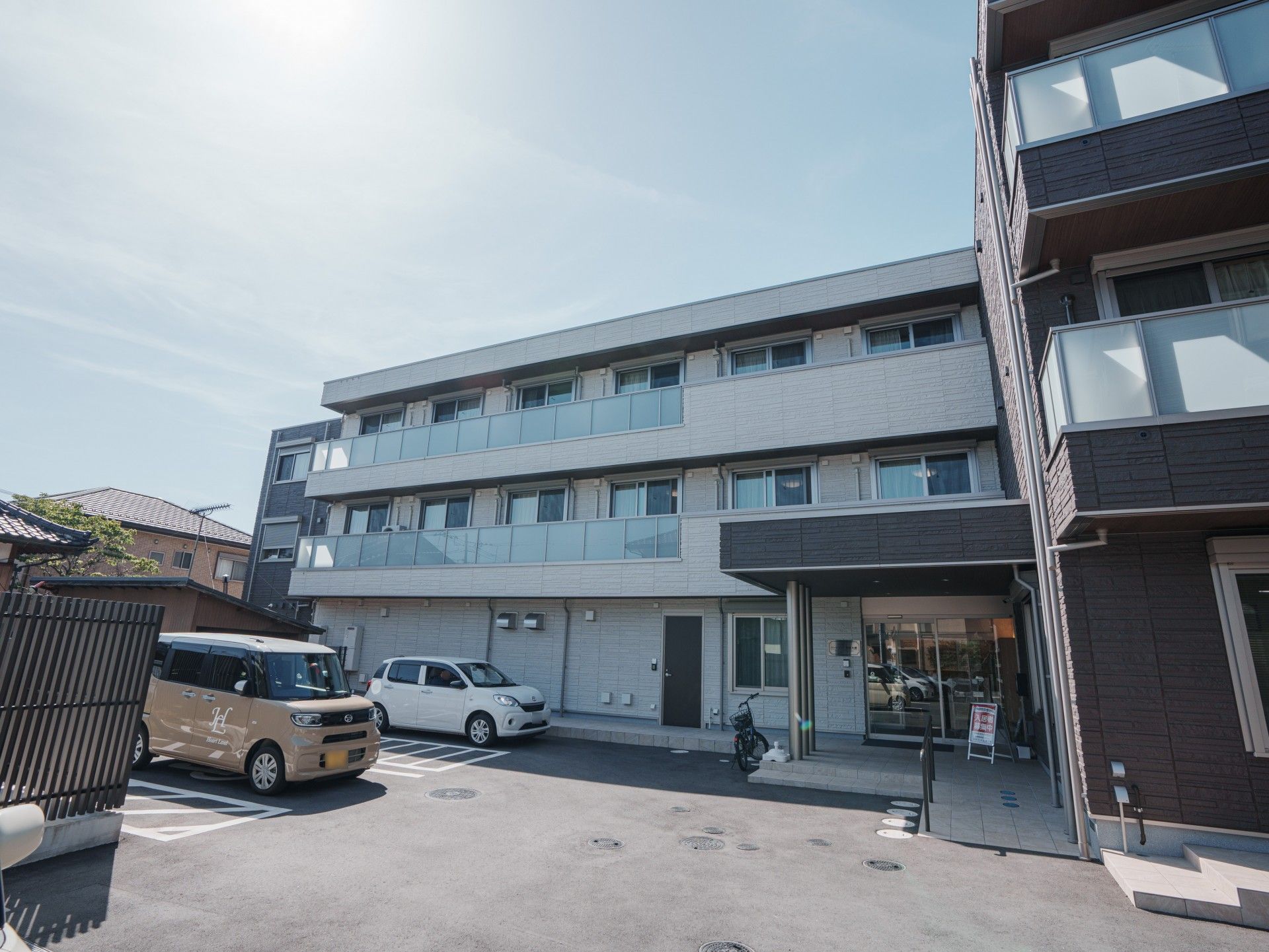 複数の車が停まっている広い駐車場。茶色と白の床の3階建ての建物。