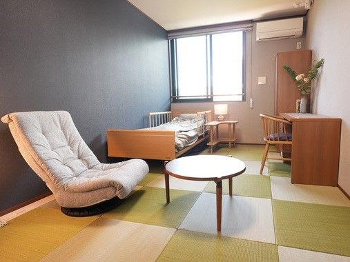 介護用ベッド、デスク、クローゼット、エアコン、丸テーブル、1人用ソファがある個室