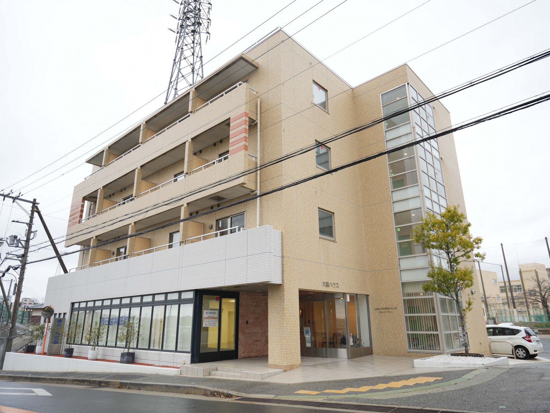 白と薄茶色のツートンカラーの外壁でバルコニーがついている4階建て建築物