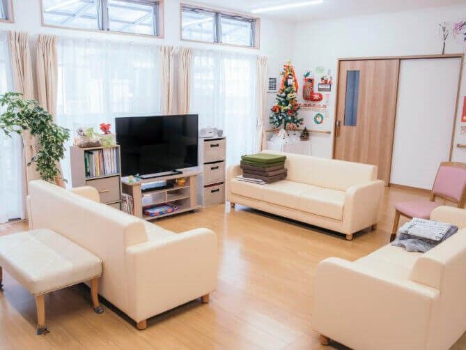 白いソファが3脚、大型テレビ1台、収納家具2組が置かれているリビング