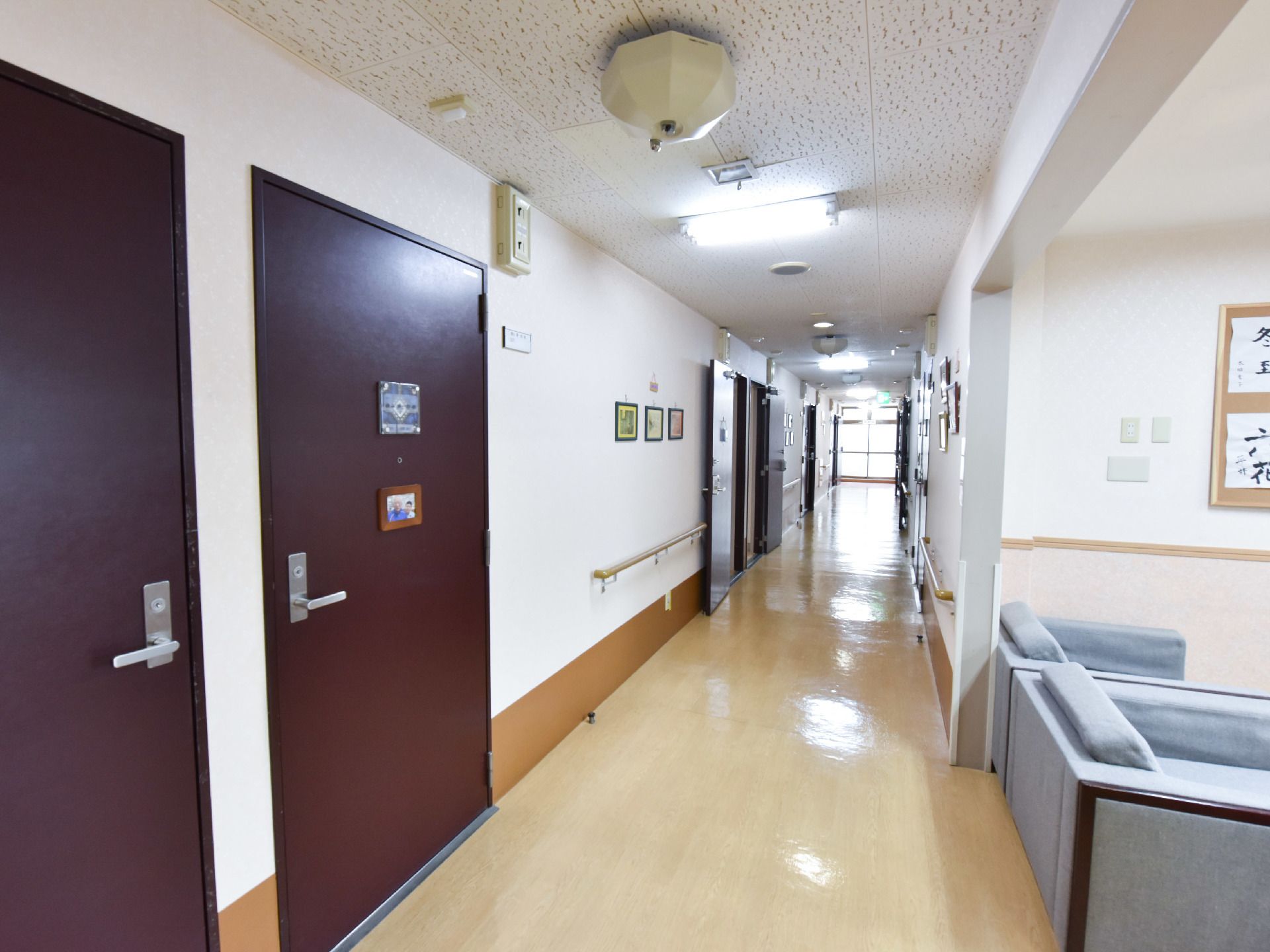 両側の壁には手すりと赤茶色の扉が設置してある。突き当たりからは光がもれており、右手前にはソファが2台置いてある。