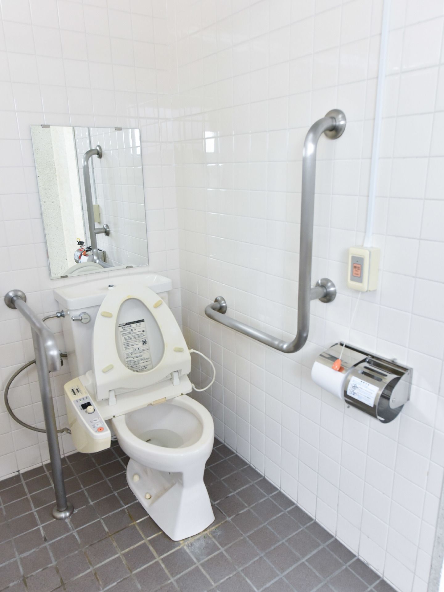 ウオッシュレットトイレの両側には手すりが設置されており右手はL字型になっている。タンクの上には鏡もついている。