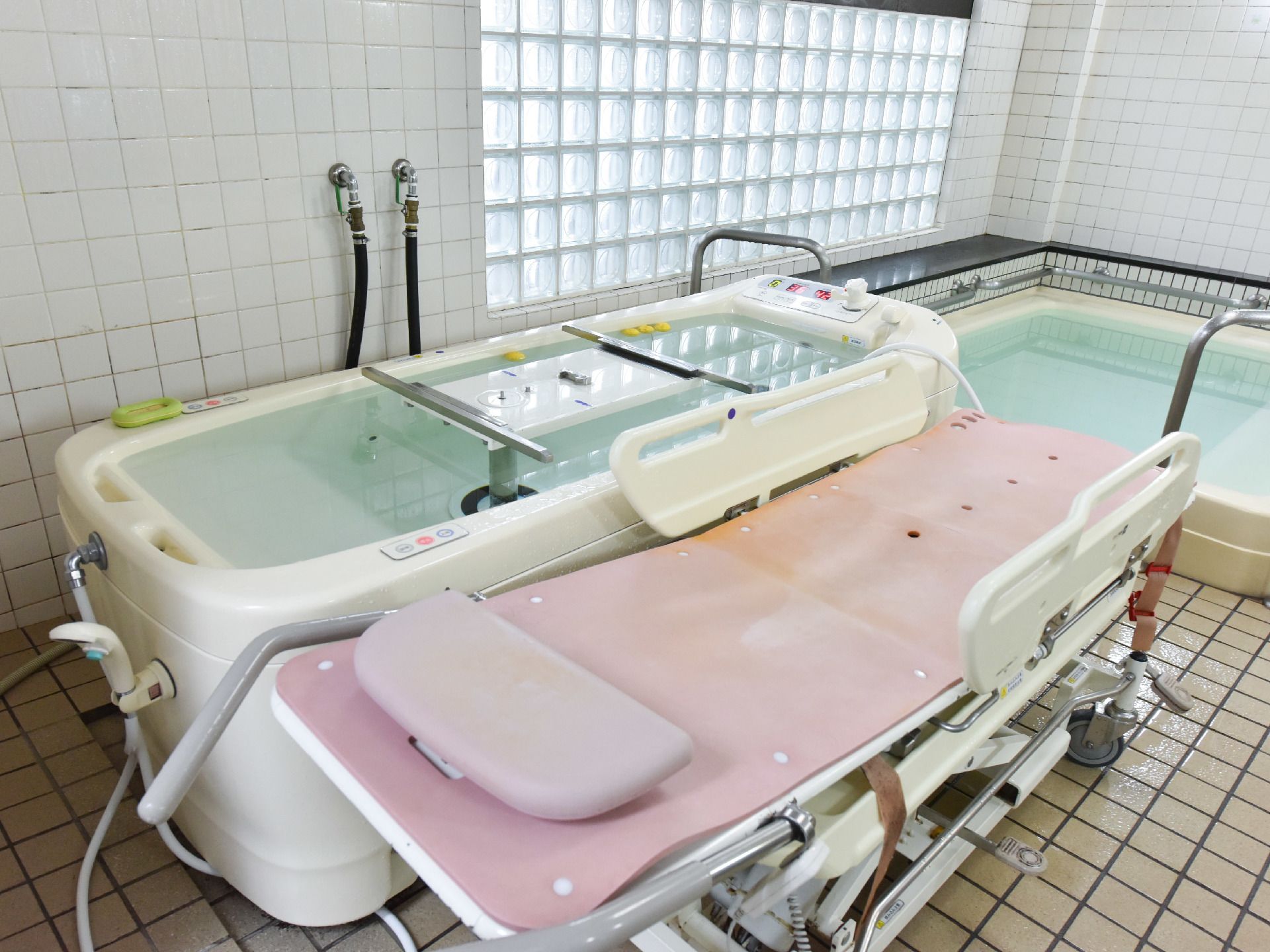 寝たままの姿勢で入浴できる介護専用器具が用意されている。床はタイル張りになっており、奥には手すり付きの浴槽も見える。