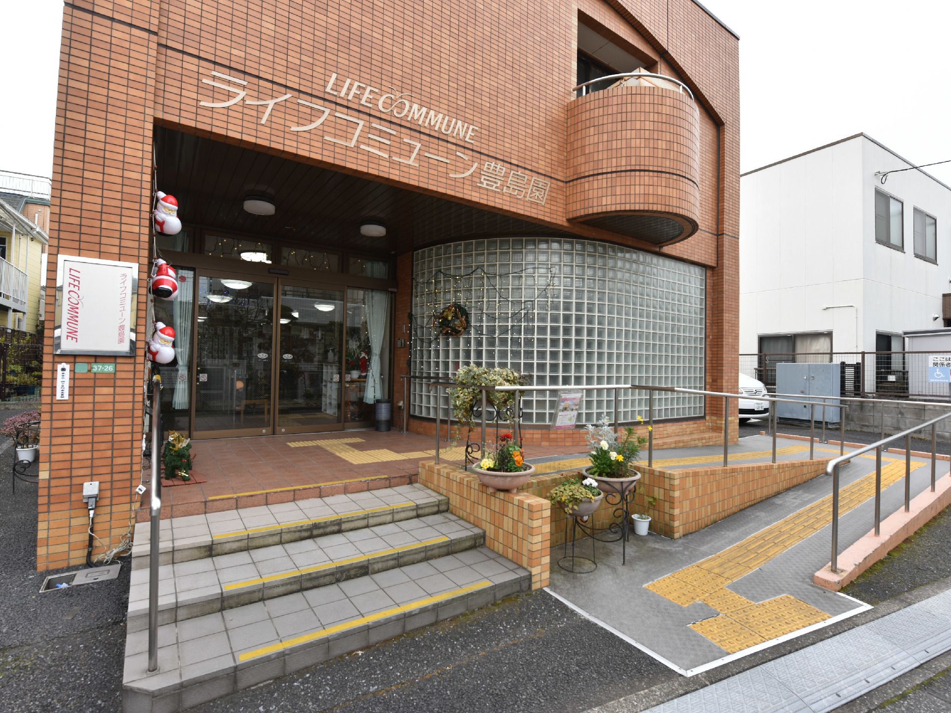 左側に入り口があり右側にスロープがついており黄色の点字ブロックが伸びている。手すりも設置されており階段もついている。