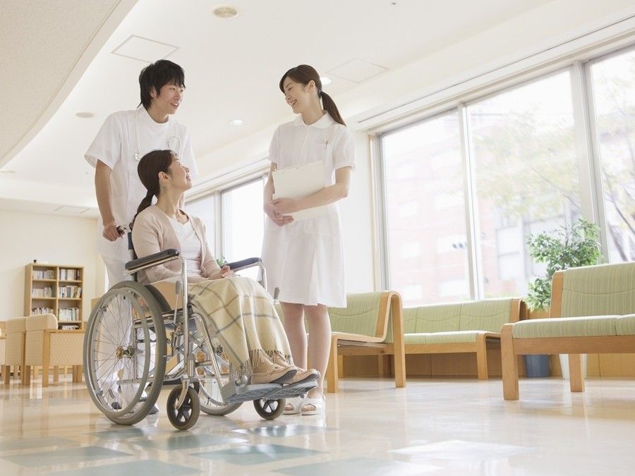 男女のスタッフと車いすに座っている女性が、親しく談笑している様子。