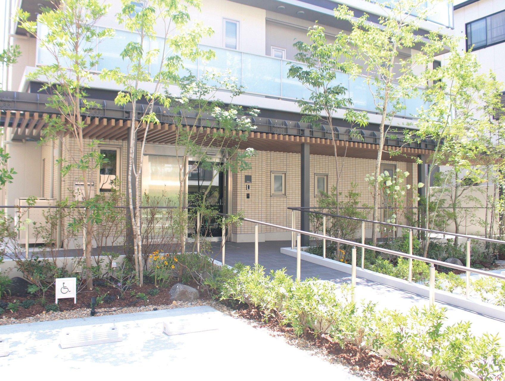 入り口付近が植物で囲まれている茶色い外壁の3階建てグループホーム