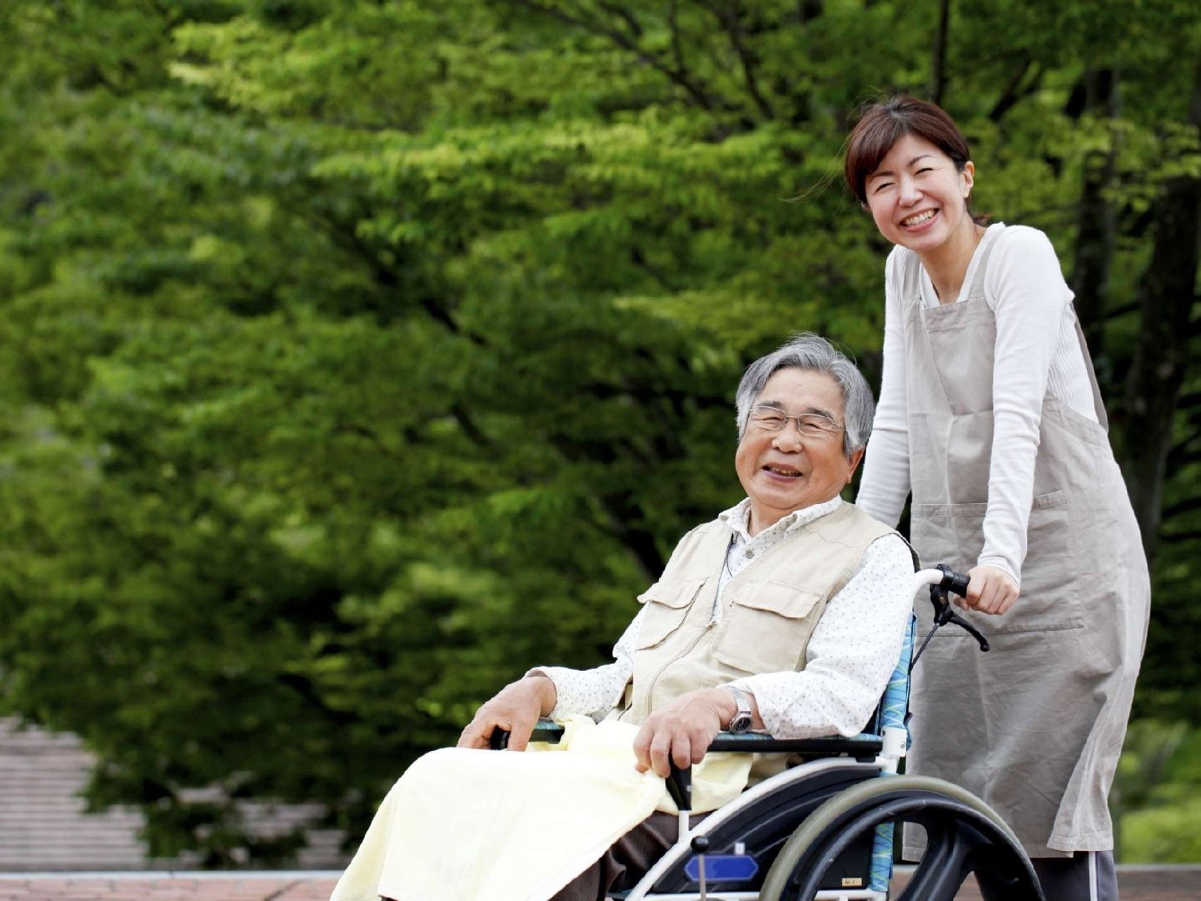 車椅子に乗った男性とその車椅子を押しているスタッフが、自然の中で景色を眺めている。