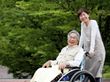 車椅子に乗った男性とその車椅子を押しているスタッフが、自然の中で景色を眺めている。