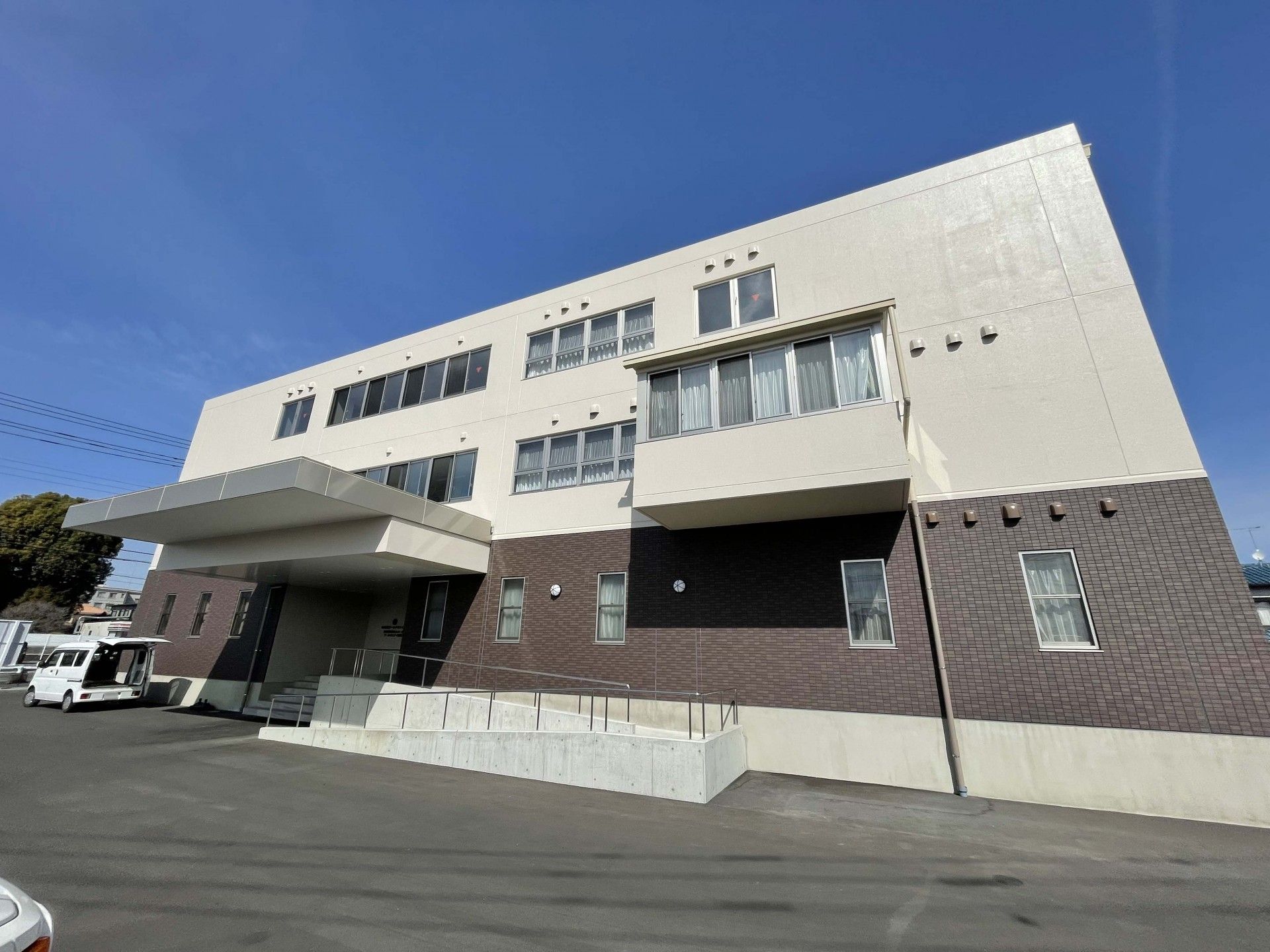 入り口に階段とスロープがある茶色とベージュの外壁の3階建て老人ホーム