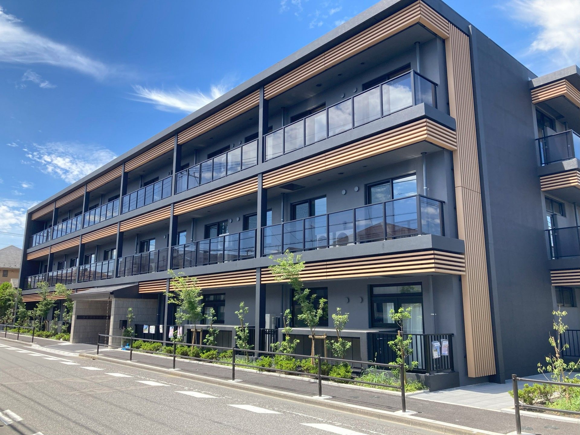 周囲が緑に囲まれており、濃いグレーの外壁のバルコニー付き3階建て建築物