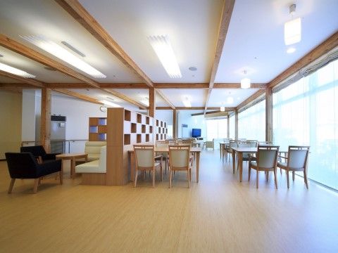 機能訓練を行う広々としたスペースと、仕切りを挟んでテレビ、椅子、テーブルが置かれた明るい雰囲気の食堂である。