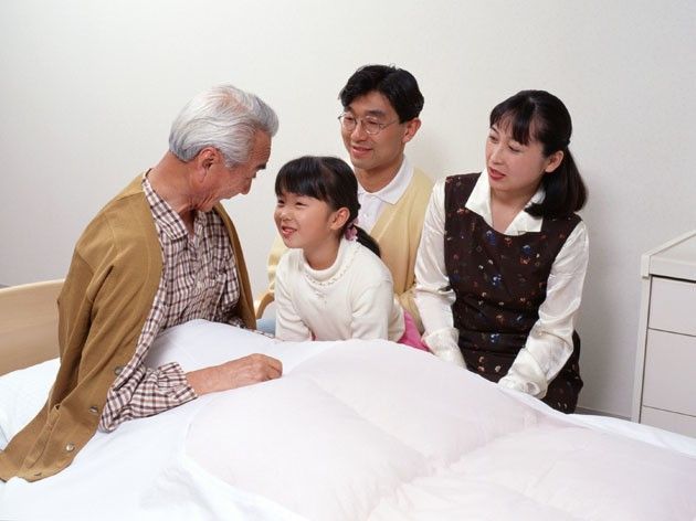 ベッド上で起き上がっている高齢の男性とお見舞いの家族