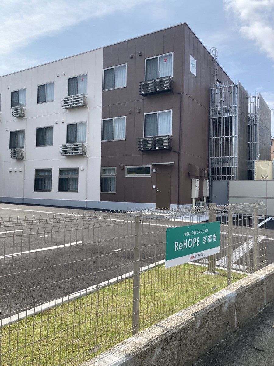 ReHOPE 京都南の看板付きフェンスがあり、茶色とアイボリーの外壁の3階建て老人ホーム