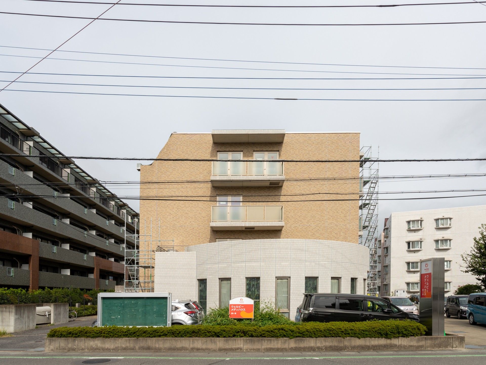 白い外壁で半円状の入り口スペースと茶色い外壁でバルコニーが見える4階建て老人ホーム