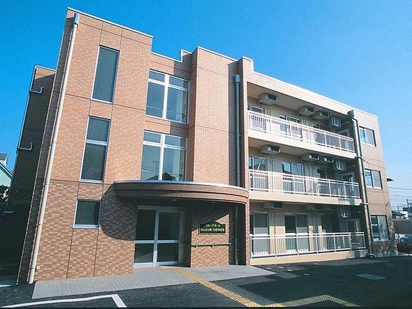 弧を描く玄関屋根が特徴的な、シックで上品な配色の3階建て施設