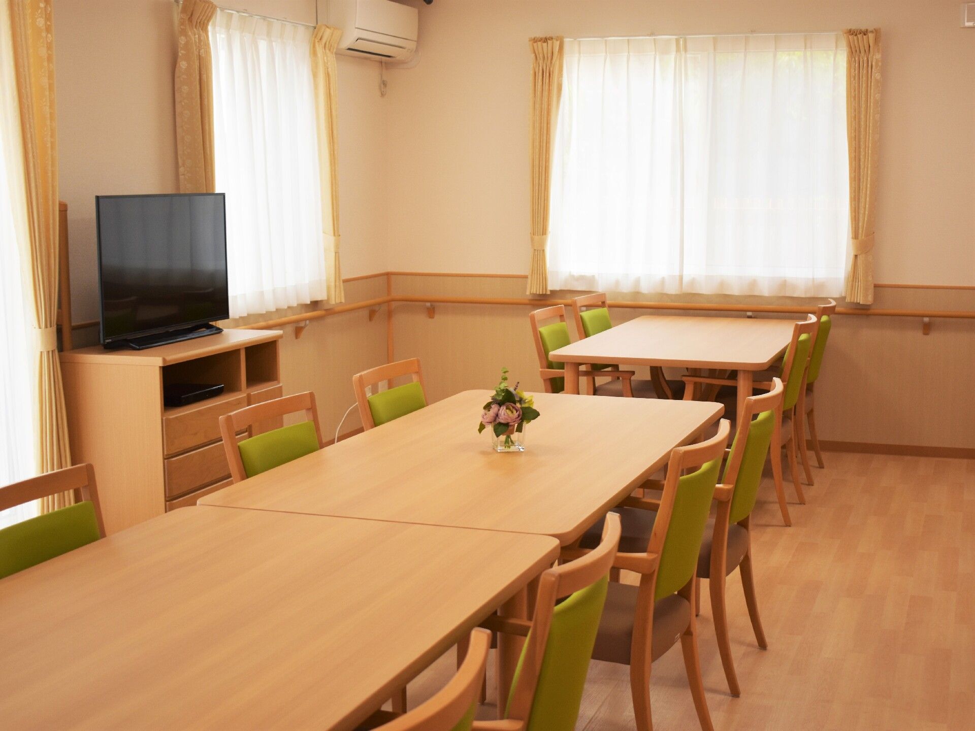 壁に手づくりの装飾や入居者様を写した多くの写真が貼られたリビング。みんなで囲めるテーブルや椅子が置かれている。