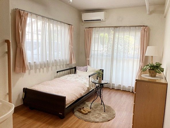 大きな窓とエアコンで、どの季節も快適に過ごせる居室である。床はフローリングで、チェストと電動介護ベッドが置かれている。