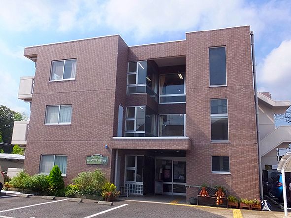 ３階建てのブラウンのマンションタイプの建物である。全ての階にはベランダが備わり、整備された駐車場がある。