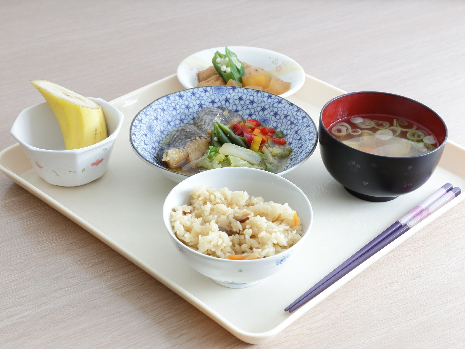 施設にて提供される一食分の食事。炊き込みご飯と味噌汁、魚を使ったメインのおかずにバナナのデザートまで付いている。